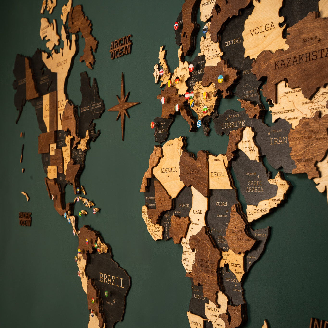 A 3D wooden map of the world with varying shades of black and brown detail, mounted on a wall.