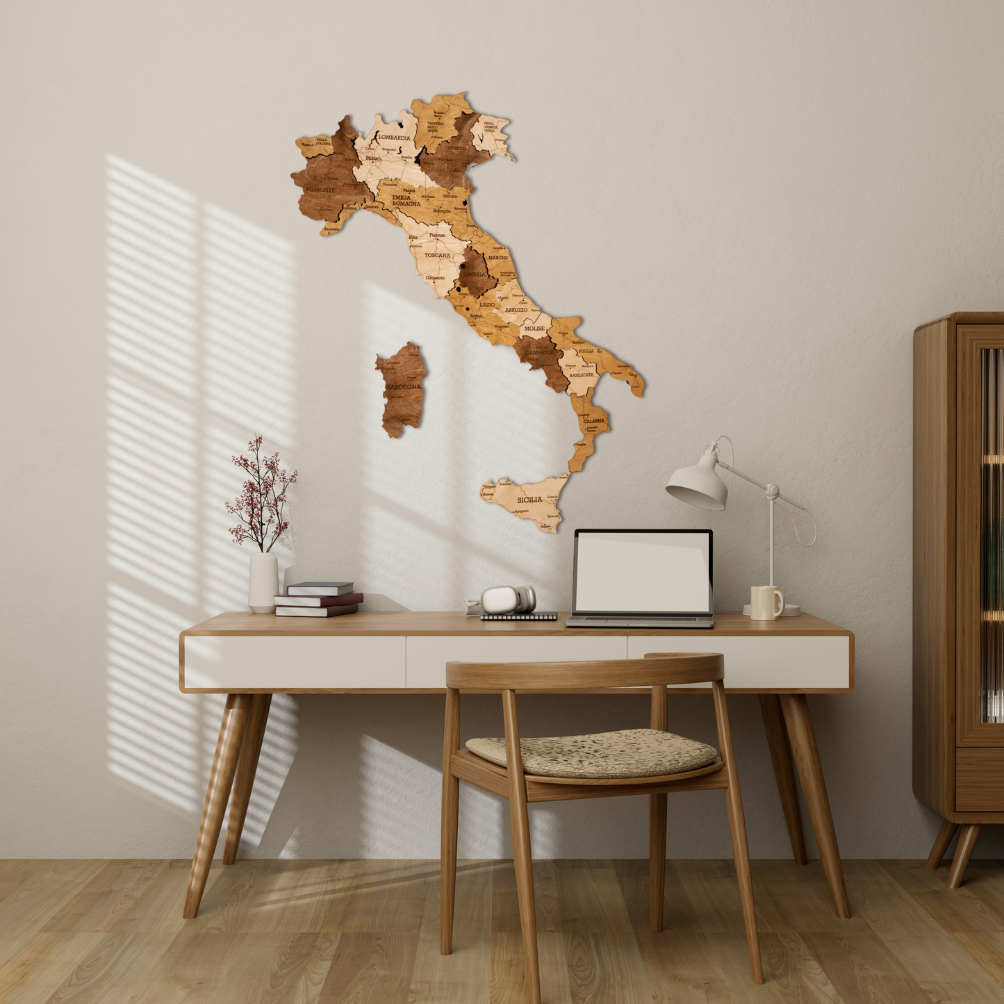 A 3D wooden map of Italy mounted on a wall above a desk with a laptop, chair, and various decor items in a room.