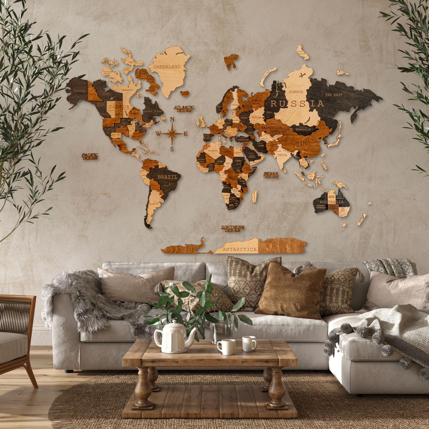 A 3D wooden world map with varying shades of brown and black, mounted on a wall above a beige sofa with cushions. The map features detailed country outlines and is displayed in a room with a concrete wall and indoor plants.